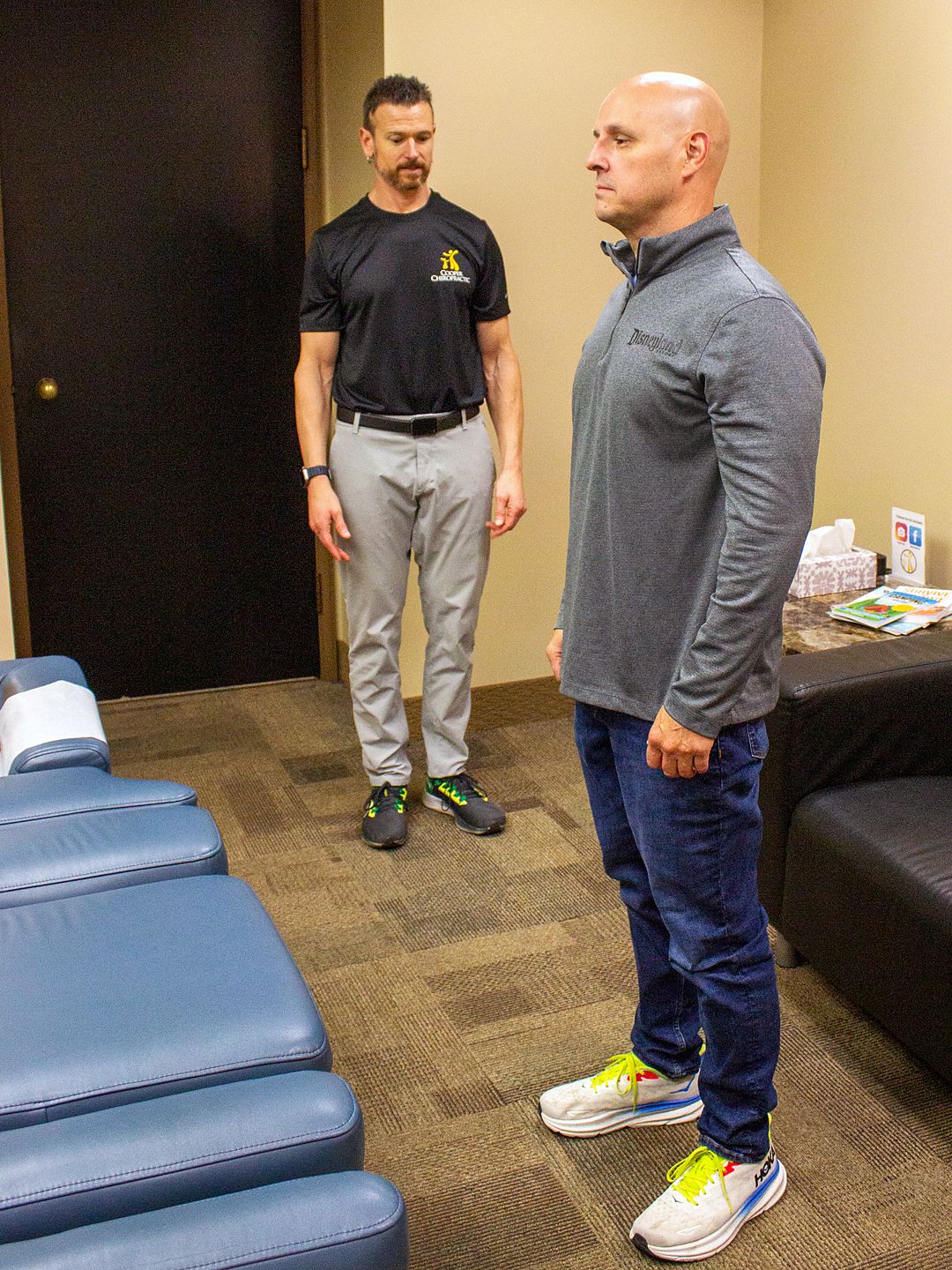 A chiropractor assessing an adult's standing posture from the side.